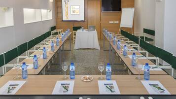 Un salón de conferencias con largas mesas, botellas de agua y vasos.