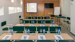 Un salón de conferencias con varias mesas, sillas y una pantalla para presentaciones.