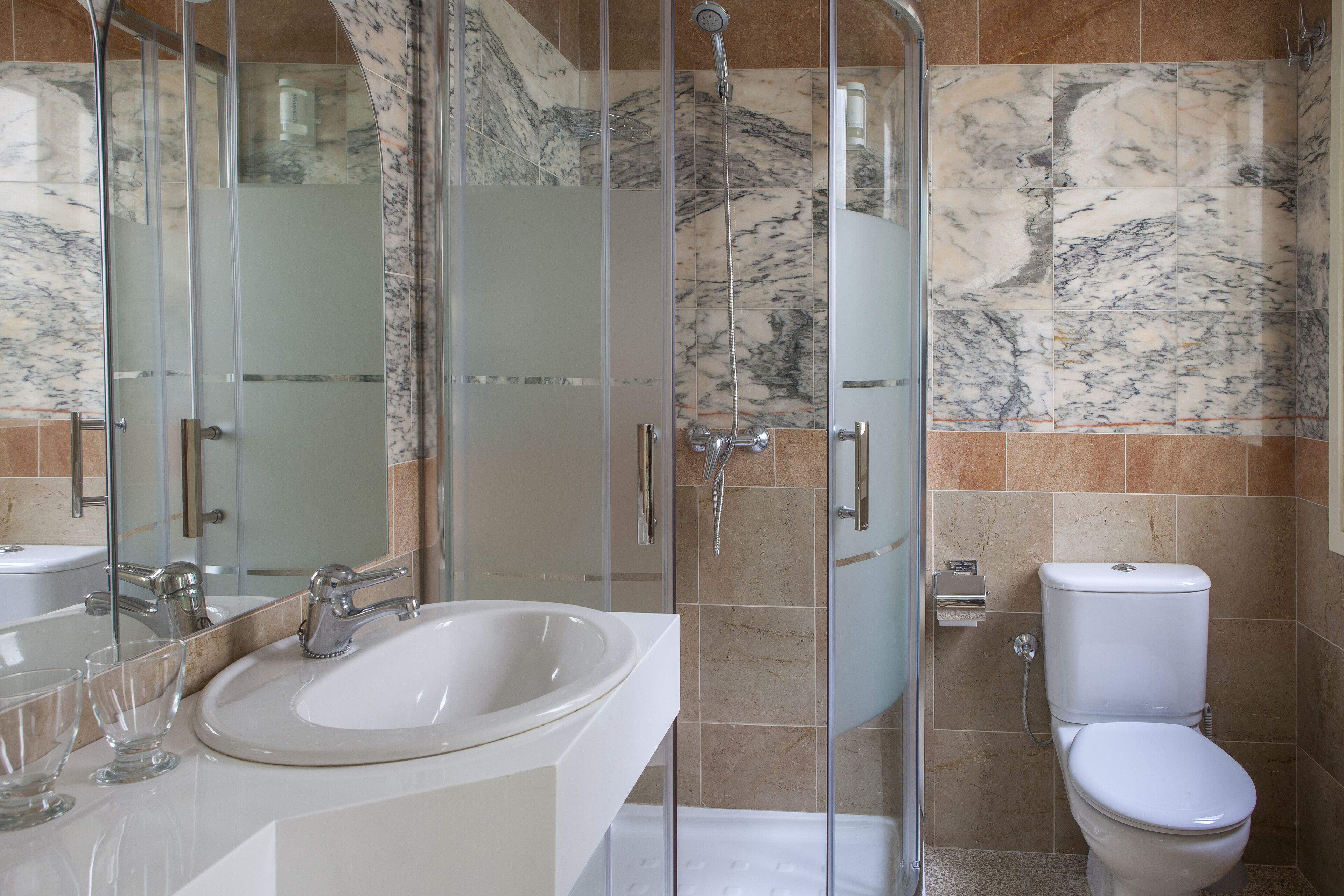 Un baño con ducha de vidrio, lavamanos blanco y retrete.