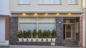 Un edificio con fachada color beige y una fila de macetas con plantas en la entrada, con un letrero que dice "AGORA".