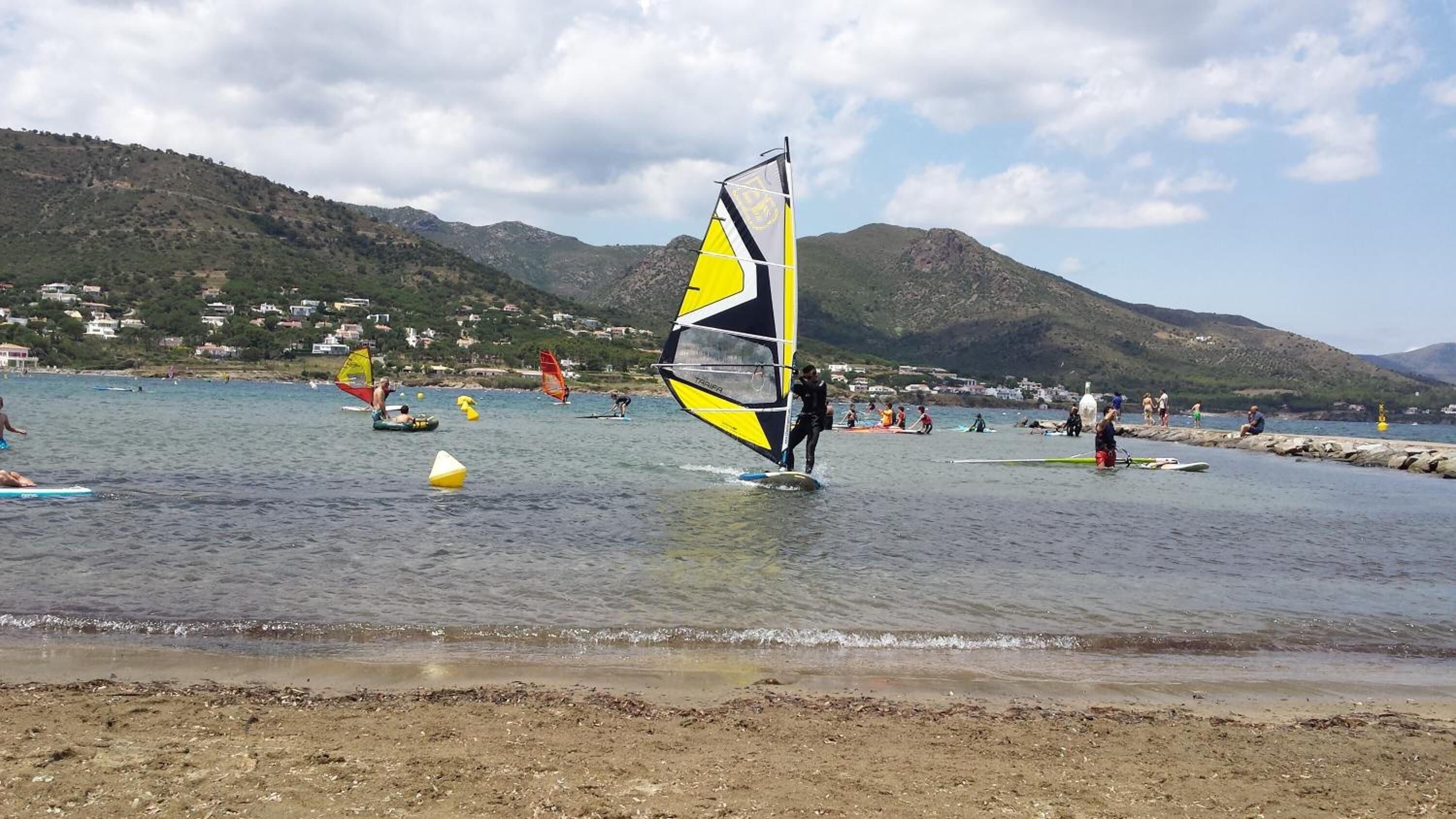 Una playa con gente practicando windsurf y nadando.