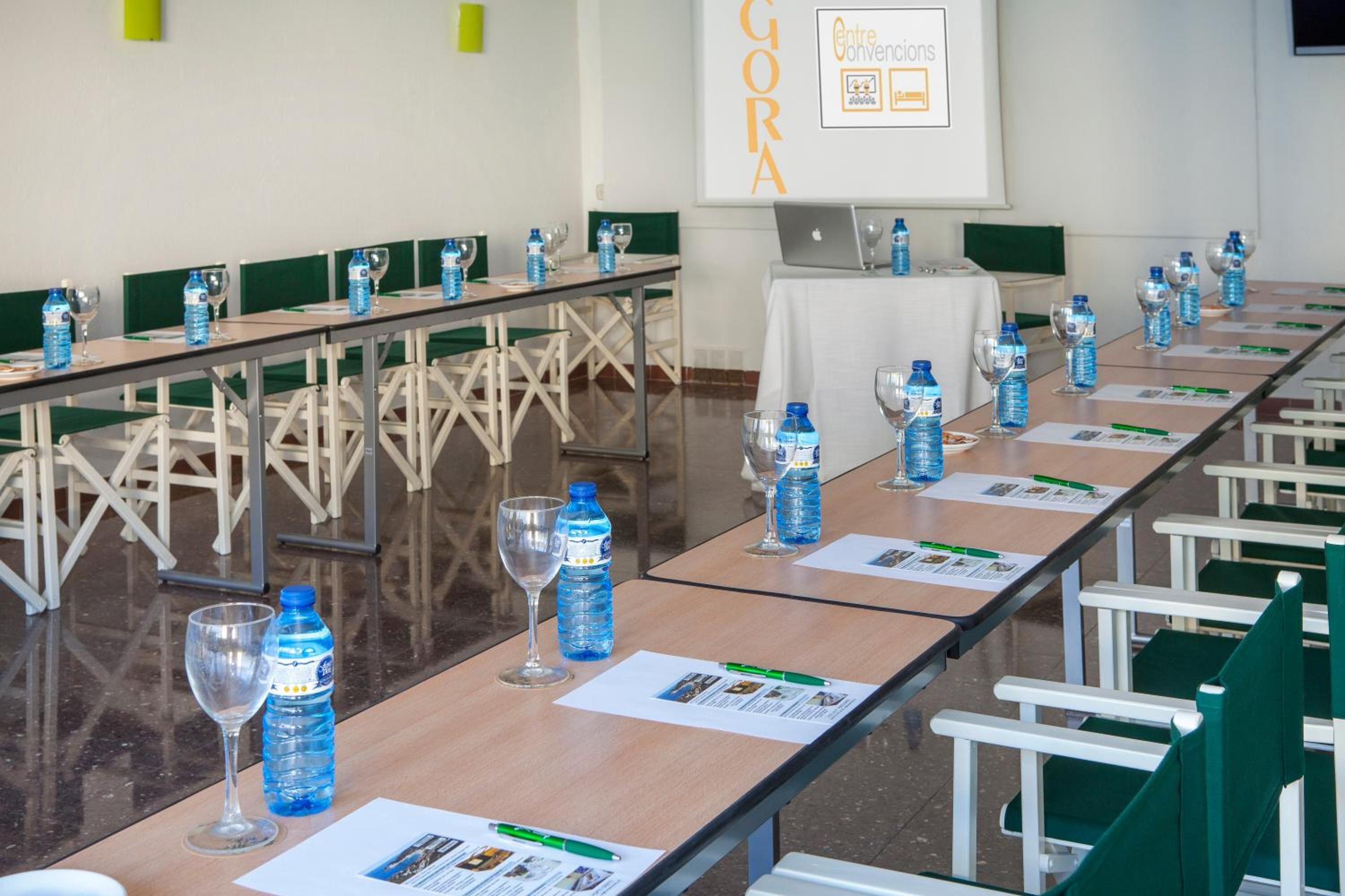 Une salle de conférence avec de longues tables, des chaises, des bouteilles d’eau et des verres.
