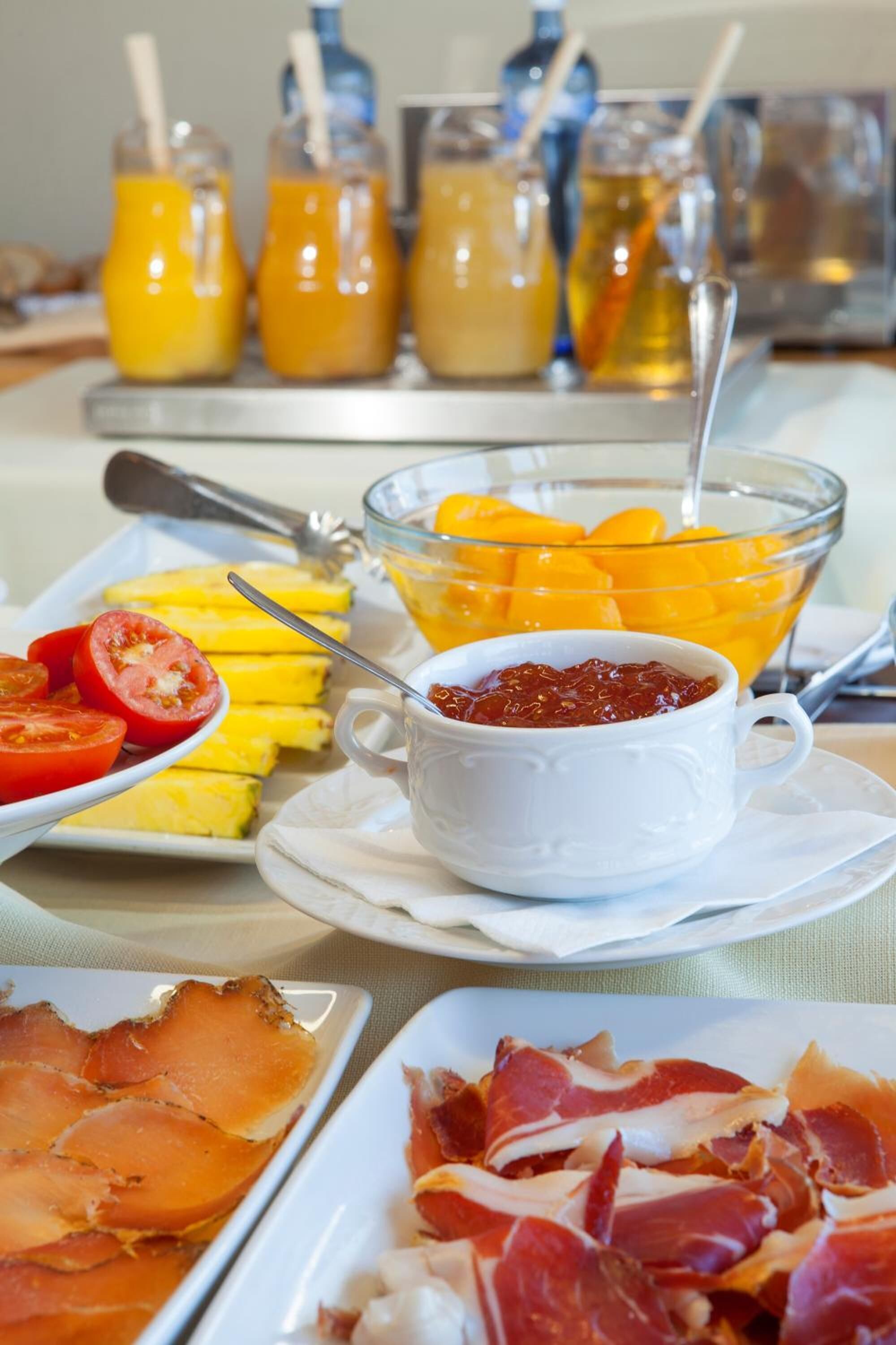 Een ontbijtbuffet met diverse producten, waaronder plakjes tomaat, mango's en een schaal jam.