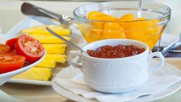 Een ontbijtbuffet met diverse producten, waaronder plakjes tomaat, mango's en een schaal jam.