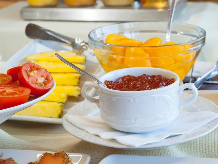 Een ontbijtbuffet met diverse producten, waaronder plakjes tomaat, mango's en een schaal jam.