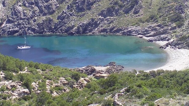 Un paisaje costero con una bahía turquesa y cristalina, acantilados rocosos y un pequeño bote anclado cerca de la orilla.