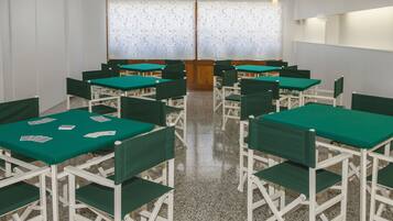 Un salón de conferencias con mesas verdes y sillas blancas, un papel tapiz decorado y un panel de madera en el centro.