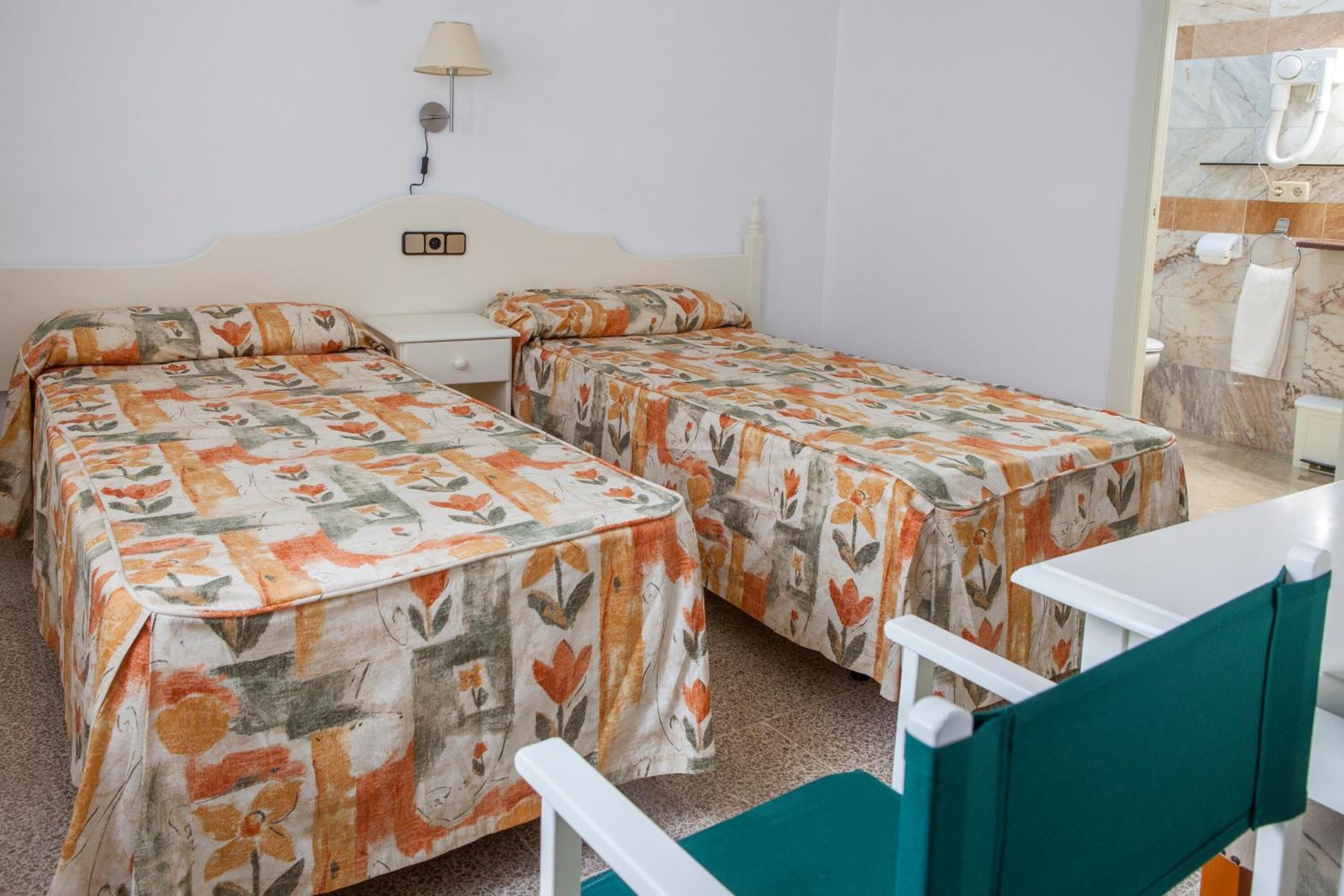 Una habitación con dos camas individuales, una mesita, una silla y un baño con pared de mármol.
