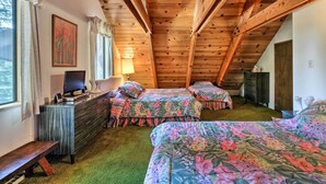 Una camera da letto mansardata accogliente con travi in legno, due letti con copriletto floreale, una scrivania con un computer e una finestra con tende.