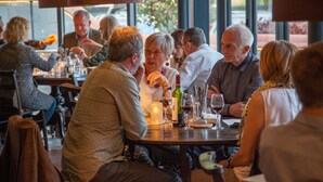 Un grupo de personas cenando en un restaurante con un amplio ventanal al fondo.
