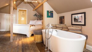 Un dormitorio con una cama grande, techo de madera, bañera y una puerta que da a otra habitación.