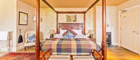Una cama con dosel y cuatro columnas, con un edredón a cuadros, dos almohadas y un banco a juego.