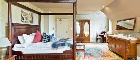 Una cama con dosel y tablero, un aparador de madera, un espejo y un tapete estampado en una habitación bien iluminada con pisos de madera.