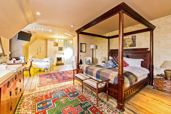 Un dormitorio amplio con cama con dosel, una zona de estar con un banco, un ventanal grande y un baño con bañera.