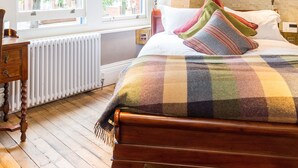 Un dormitorio con una cama de madera, una ventana con vistas a árboles, un radiador y una mesita de noche de madera con una lámpara.