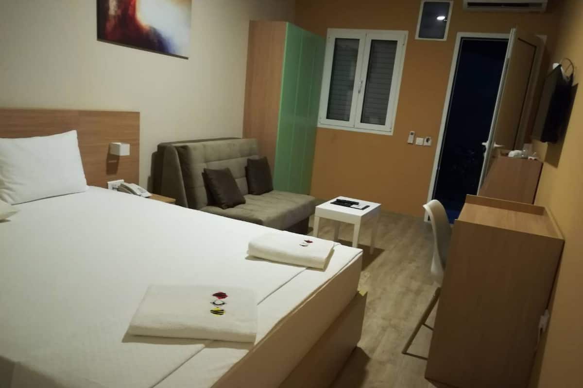 A hotel room with a large bed, a small sofa, a desk, and a wardrobe.