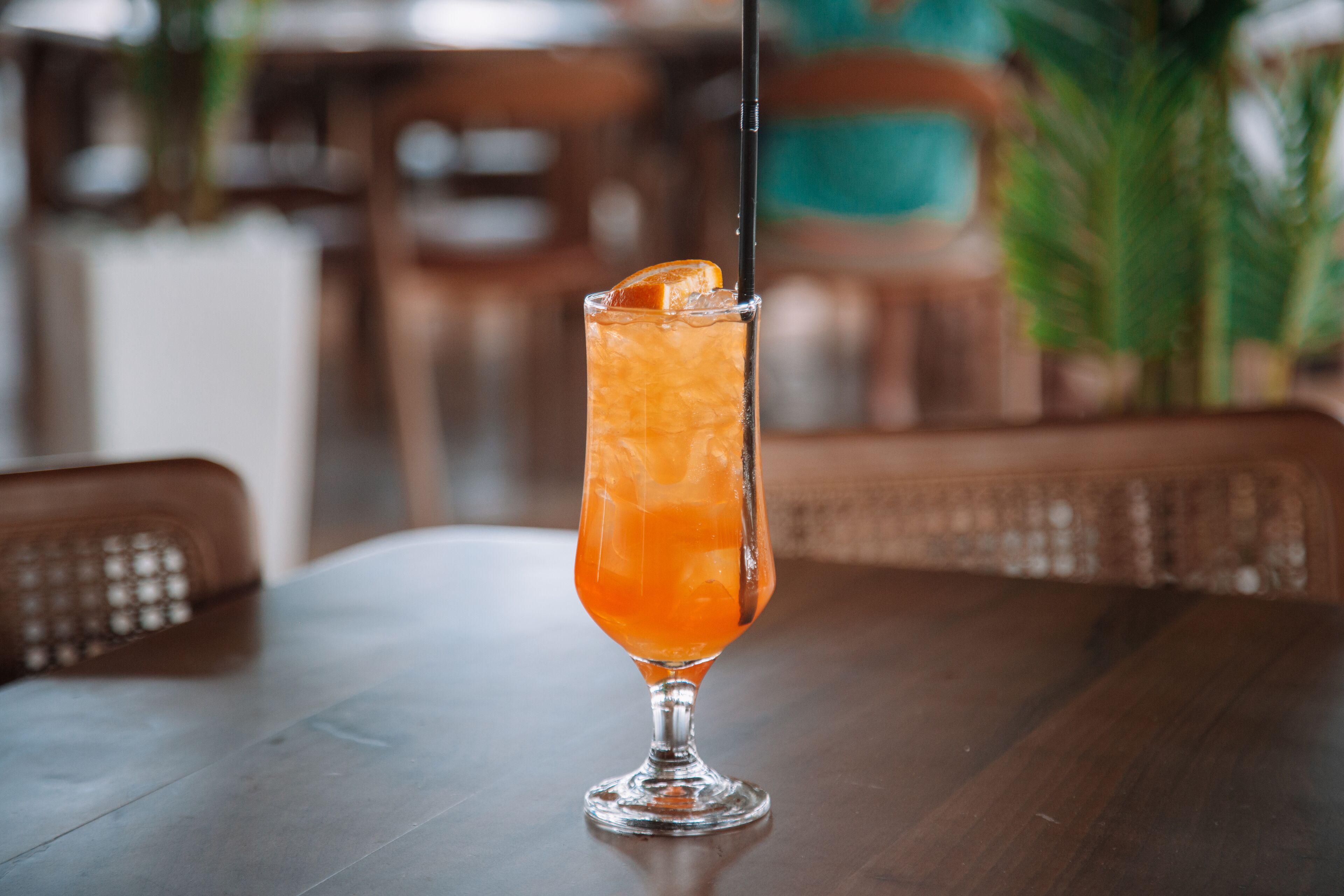 A tall glass with a drink on a wooden table in a restaurant.