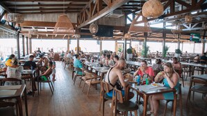 Un restaurant spacieux avec des tables et des chaises en bois, de grandes lampes en osier suspendues et une vue sur la ville grâce à de larges fenêtres.