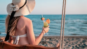 Une personne assise sur une balançoire en bois, d’où l’on aperçoit une plage et l’océan en arrière-plan.