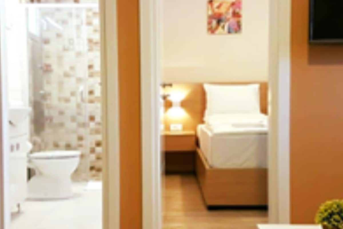 A hotel room with a bathroom, a bed, a bedside table, and a TV.