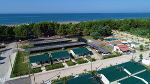 Vue aérienne d’une station balnéaire avec plusieurs cabanes aux toits végétalisés, une piscine et des parasols de plage.