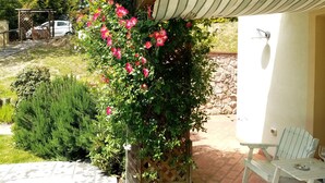 A patio area with a wooden table and chairs, a stone wall, and a pergola with climbing plants. - villa in the green | street number 2 (uzzano)