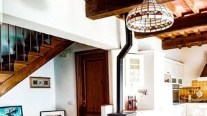 A living room with a wooden staircase, a TV, a small table, and a kitchen area visible through an open door. - villa in the green | street number 2 (uzzano)