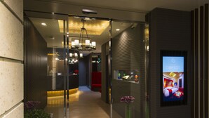 Eine moderne Hotellobby mit Glastrennwand, einer Rezeption, einer Kristallleuchtre und einem digitalen Bildschirm.