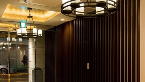 Eine moderne Lobby mit einer Wand aus Holzlamellen, einem Glastürbereich und einer Kristallleuchtre.'