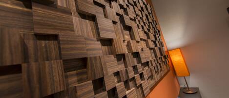 A wall with a geometric wooden panel design, a bedside table with a lamp, and a bedside drawer.