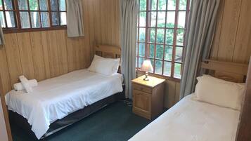 A room with two beds, a nightstand with a lamp, and large windows with curtains.