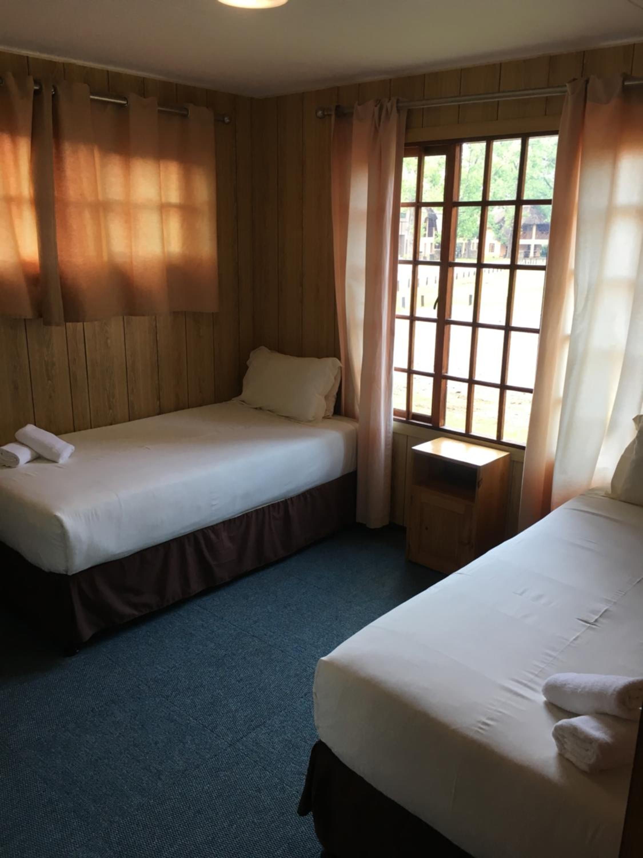 Una habitación con dos camas individuales, una mesita y un ventanal con cortinas.