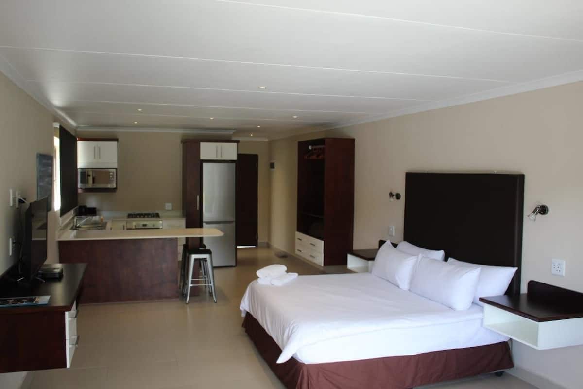 A hotel room with a bed, a desk, a kitchenette, and a TV.