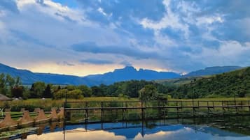 Un paysage paisible avec une étendue d’eau qui reflète le ciel, un pont en bois et des montagnes lointaines sous un ciel nuageux.