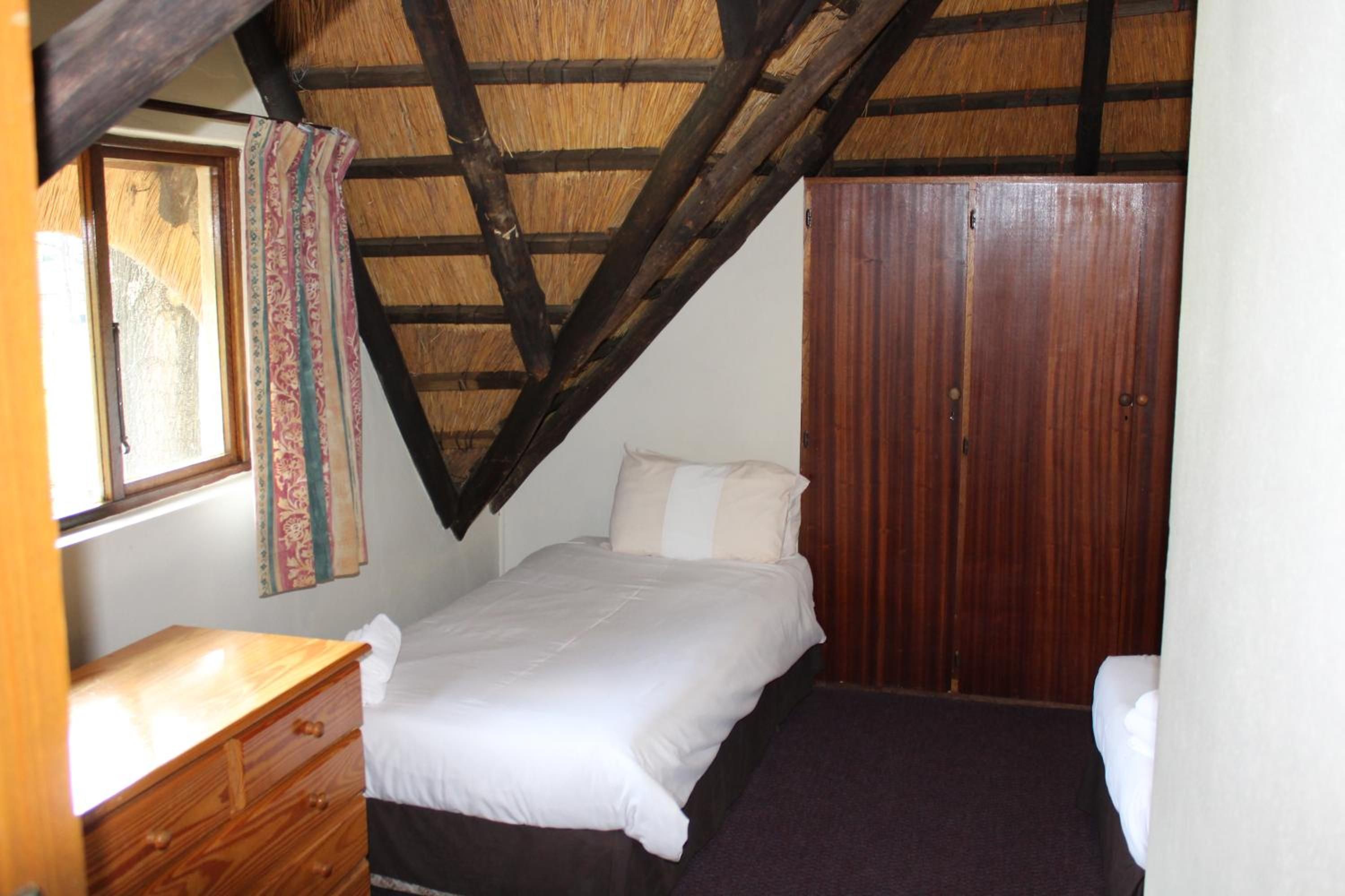 A bedroom with a bed, a wooden dresser, a wardrobe, and a window with curtains.