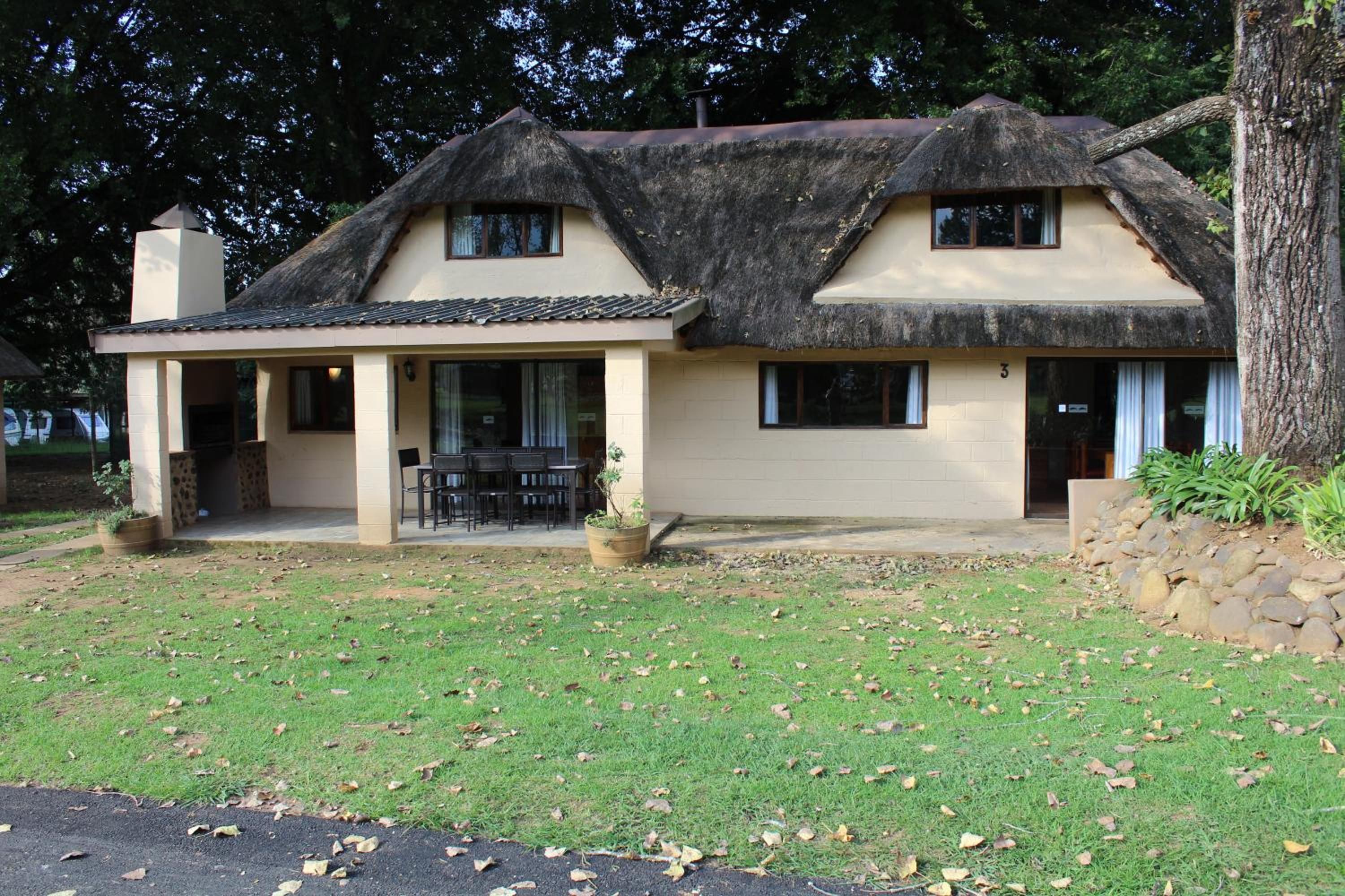 A two-story house with a thatched roof, a covered porch, and a stone wall.
