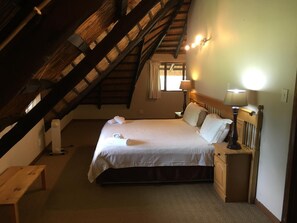Un lit simple avec une tête de lit en bois et des tables de chevet, un banc et un plafond en pente avec des poutres apparentes.