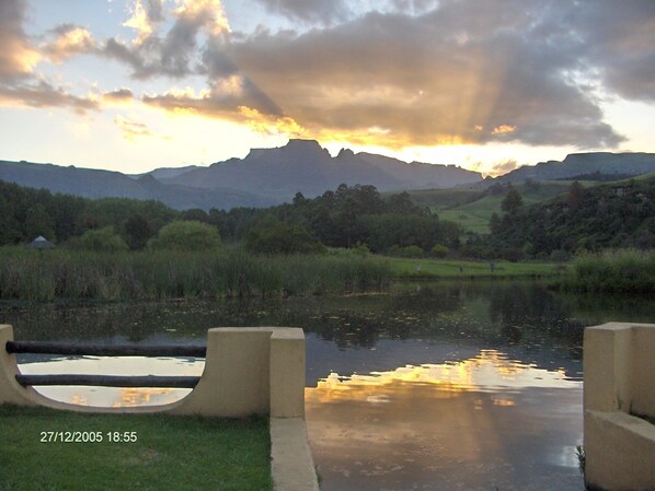 A serene landscape with a body of water reflecting the sky, surrounded by greenery and distant mountains.