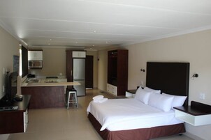 A hotel room with a bed, a desk, a kitchenette, and a TV.