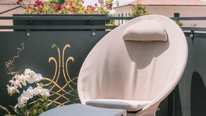 A round, cushioned chair with a small table, positioned on a tiled patio with a decorative fence and potted plants in the background. - Little House (Campo San Martino)
