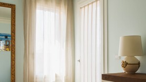 A hotel room with a bed, a desk, a lamp, a mirror, and a window with sheer curtains. - Little House (Campo San Martino)