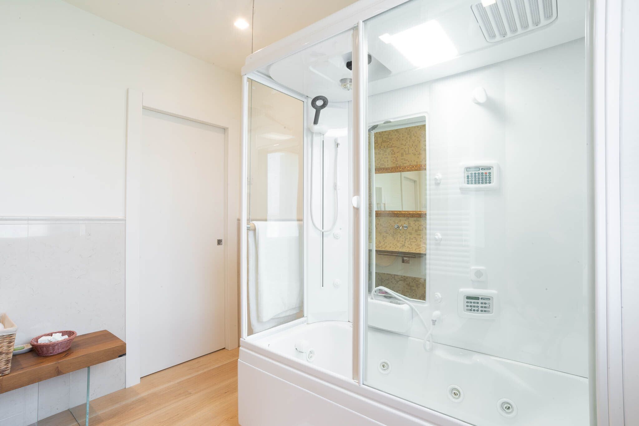 A modern bathroom with a glass-enclosed shower, a built-in toilet, and a wooden shelf with a basket.