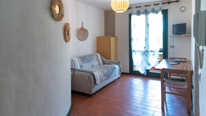 A living room with a sofa, a dining table, a television, and a hanging light fixture. - Residence Pinnetta - 4-seater apartment with free pool and WiFi (Arzachena)