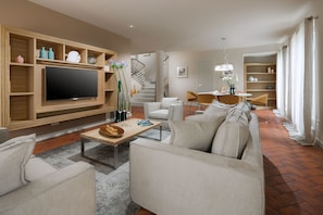 A modern living room with a flat-screen TV, a sofa, a coffee table, and a staircase leading to another level.