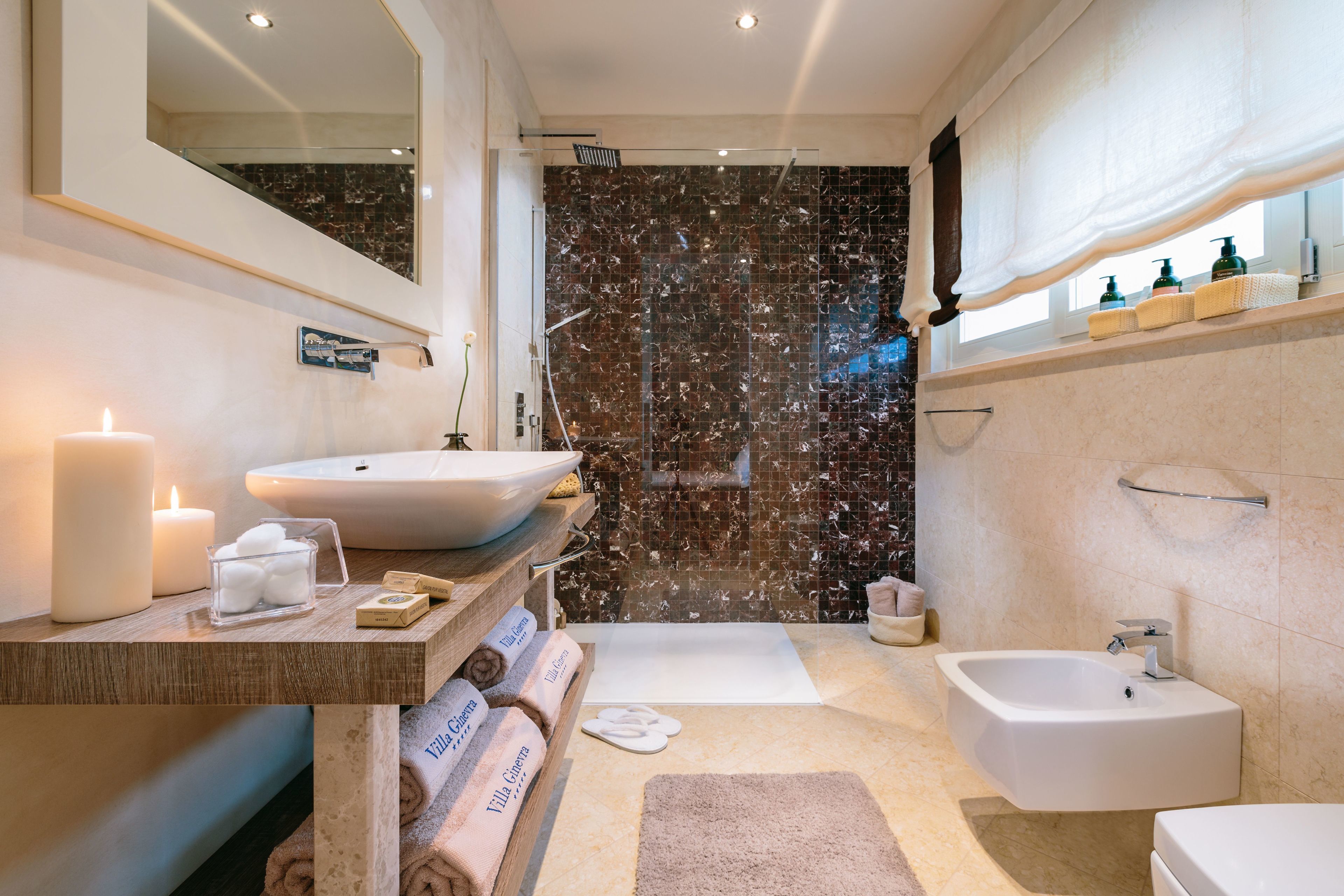 A modern bathroom with a marble shower wall, a large sink, a bathtub, and a separate sink.