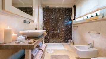 A modern bathroom with a marble shower wall, a large sink, a bathtub, and a separate sink.