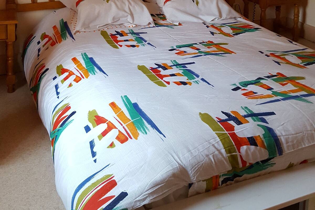 Una cama con colcha colorida, cabecera de madera, mesitas de noche y un cuadro enmarcado en la pared.
