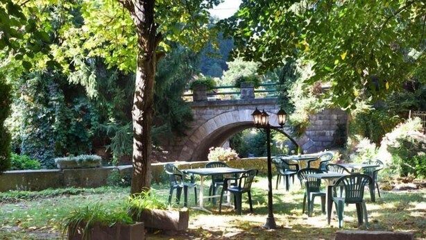 Un área de estar al aire libre con mesas y sillas, un puente de piedra y abundante vegetación.