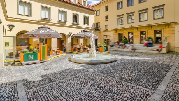 A courtyard with cobblestone flooring, a central fountain, and outdoor seating areas with umbrellas. - Apartment Charles Bridge (Prague)