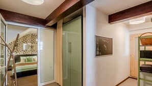 A modern hotel room with a glass door closet, a bed with a geometric-patterned headboard, and a wall-mounted artwork. - Apartment Charles Bridge (Prague)
